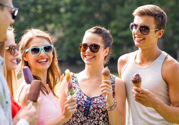 concepto de amistad, ocio, dulces, verano y gente - grupo de amigos sonrientes con helado al aire libre