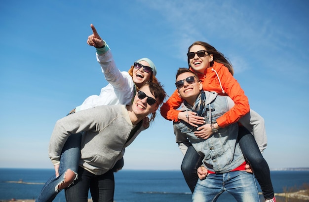 concepto de amistad, ocio y personas - grupo de amigos adolescentes felices con gafas de sol divirtiéndose al aire libre