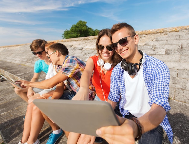 concepto de amistad, ocio, verano y personas - grupo de amigos sonrientes con computadoras tablet pc sentados al aire libre