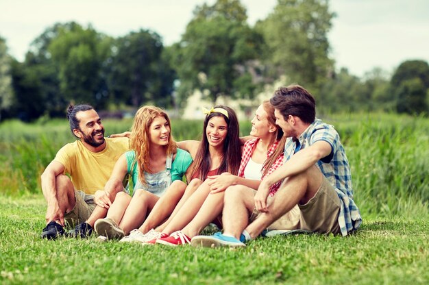 concepto de amistad, ocio, verano y personas - grupo de amigos sonrientes sentados en el césped y hablando al aire libre