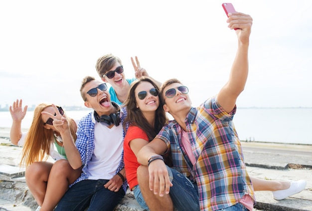 concepto de amistad, ocio, verano, tecnología y personas - grupo de amigos felices con smartphone tomando selfie al aire libre