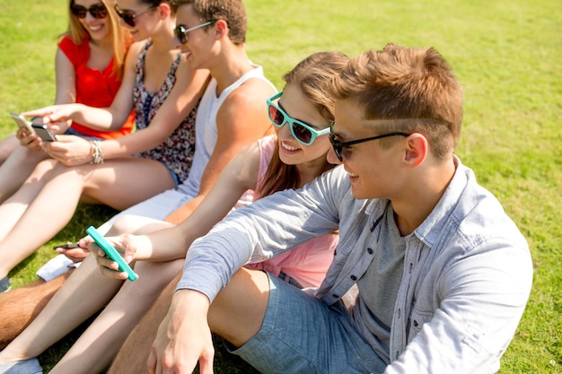 concepto de amistad, ocio, verano, tecnología y personas - grupo de amigos sonrientes con smartphone sentados en el césped y haciendo selfie en el parque