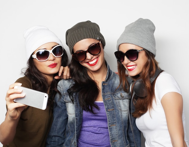 Concepto de amistad, personas y tecnología: tres adolescentes felices con smartphone tomando selfie