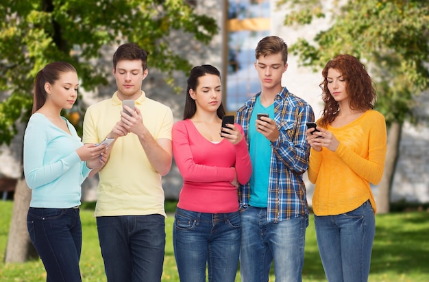 concepto de amistad, tecnología, educación, escuela y personas - grupo de adolescentes serios con smartphones sobre el fondo del campus