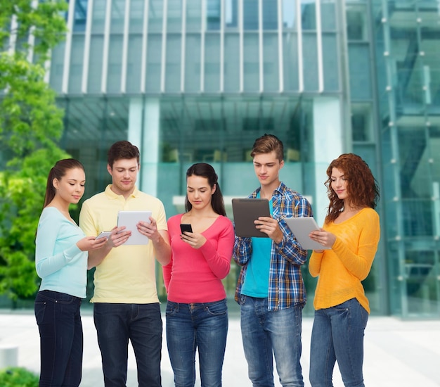 concepto de amistad, tecnología, educación, negocios y personas - grupo de adolescentes sonrientes con teléfonos inteligentes y tabletas sobre el fondo del campus