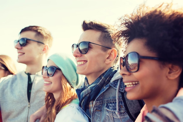 concepto de amistad, turismo, viajes y personas - grupo de amigos adolescentes felices con gafas de sol abrazándose al aire libre