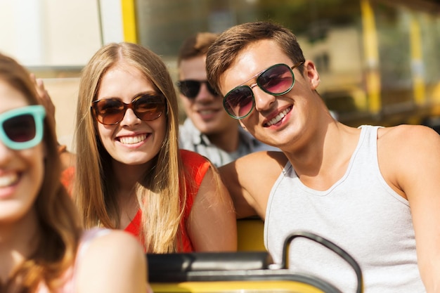 concepto de amistad, viajes, vacaciones, verano y personas - grupo de amigos adolescentes sonrientes y pareja con gafas de sol viajando en autobús turístico