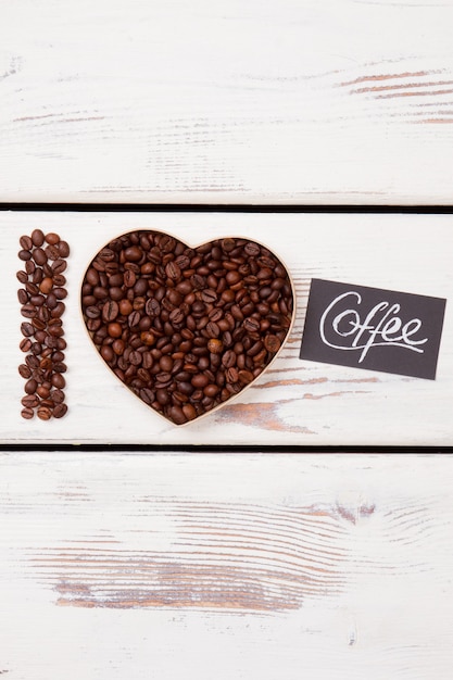 Foto concepto de amor de café. granos de café laicos planos dispuestos en forma de corazón y la palabra i. madera blanca en la superficie.