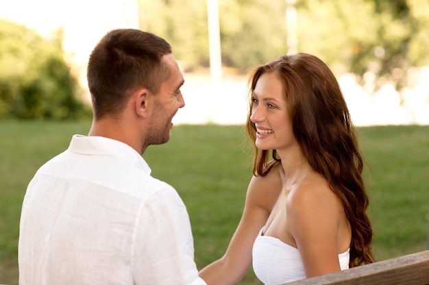 concepto de amor, citas, personas y amistad - pareja sonriente sentada en un banco y mirándose en el parque