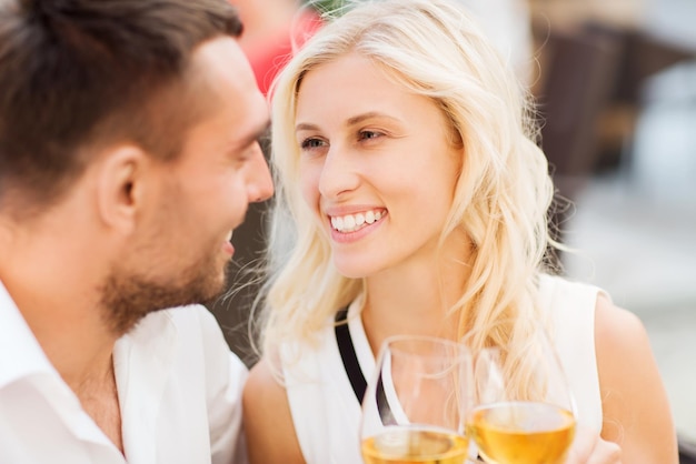 concepto de amor, citas, personas y vacaciones - pareja sonriente tomando copas de vino y mirándose en el salón del restaurante o en la terraza