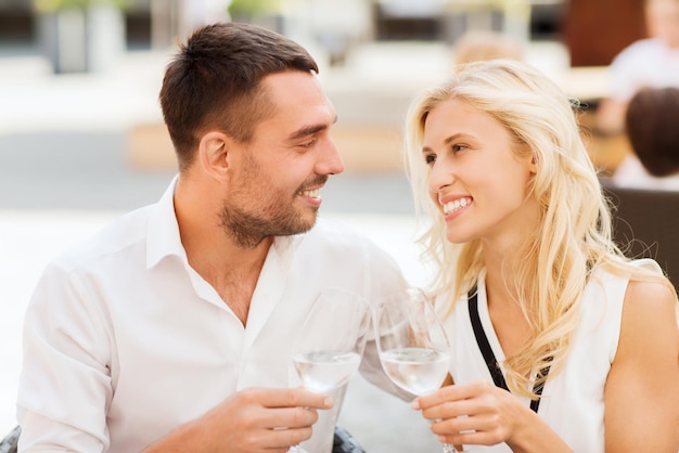 concepto de amor, citas, personas y vacaciones - pareja sonriente tomando vasos y mirándose el uno al otro en el salón del restaurante o en la terraza