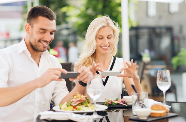 concepto de amor, fecha, tecnología, personas y relaciones - pareja feliz con smatphone tomando fotos de la comida en el restaurante