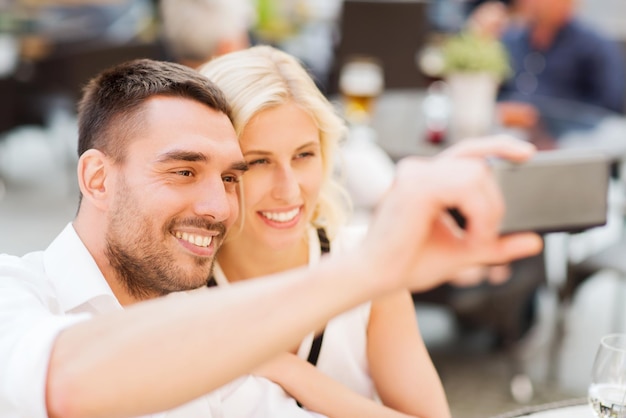 concepto de amor, fecha, tecnología, personas y relaciones - pareja feliz sonriente tomando selfie con smartphone en el café de la calle de la ciudad