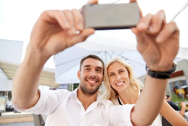 concepto de amor, fecha, tecnología, personas y relaciones - pareja feliz sonriente tomando selfie con smatphone en la terraza del restaurante