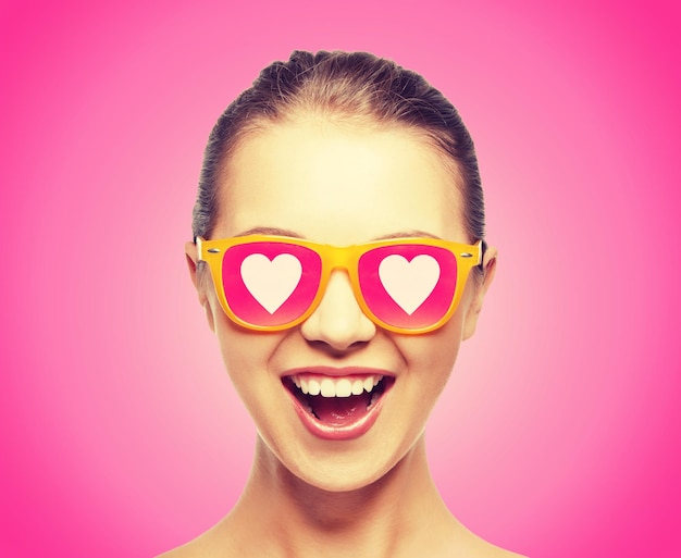 El concepto de amor, felicidad y día de San Valentín: una adolescente sorprendida con gafas de sol con corazones de fondo rosa