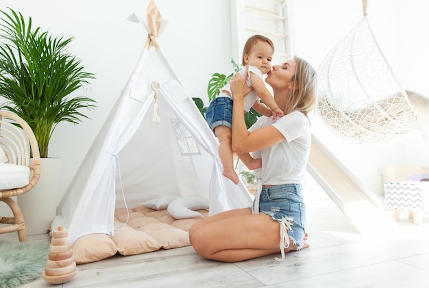 Concepto de amor maternal Mamá abraza y besa a su hija pequeña en la mejilla en una habitación con wigwam