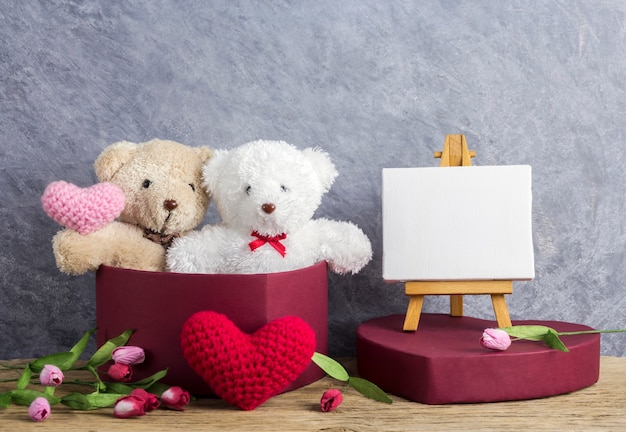 Concepto de amor de oso de peluche en caja de regalo de corazón rojo y marco de lona en blanco sobre pintura de caballete