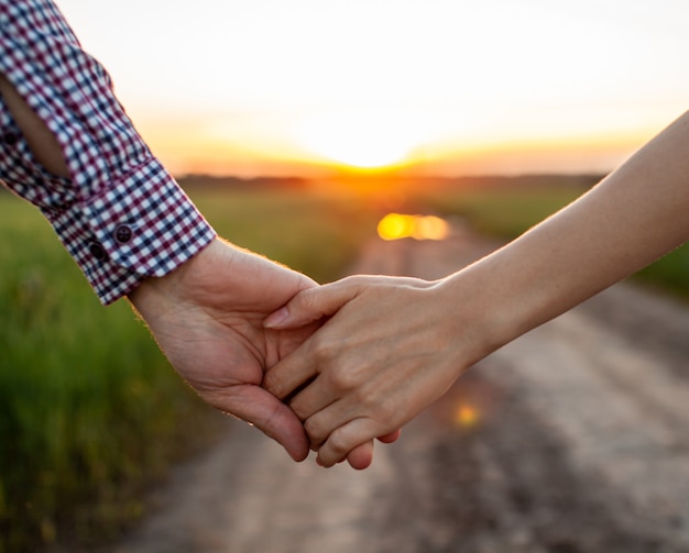 Concepto de amor. Una pareja cogidos de la mano durante la puesta de sol, símbolo de amor y relación feliz. Una joven pareja enamorada camina por un campo al atardecer, tomados de la mano y mirando la puesta de sol