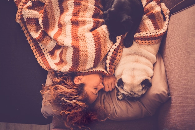 Concepto de amor con perros, animales y personas: una hermosa y dulce mujer duerme en casa en el sofá con sus dos adorables mejores amigos pugs cerca de ella para simular y disfrutar de la amistad. concepto de terapia con mascotas