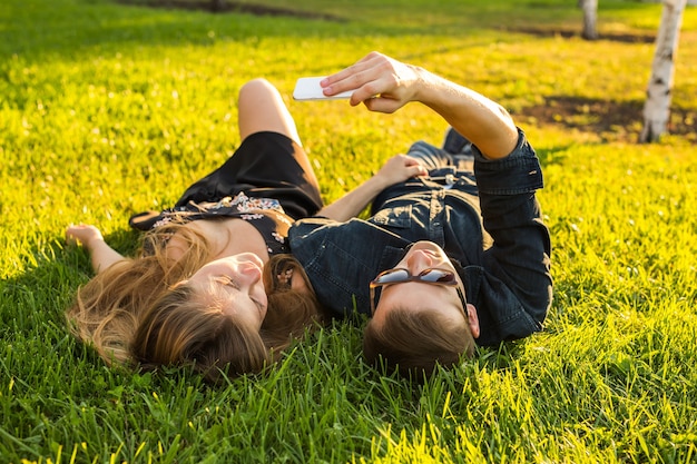 Concepto de amor y personas - feliz pareja adolescente tumbado en la hierba y tomando selfie en smartphone en verano.