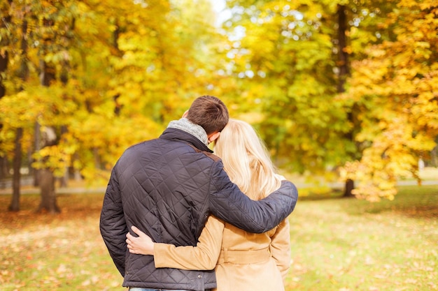 concepto de amor, relación, familia y personas - pareja abrazándose en el parque de otoño desde atrás