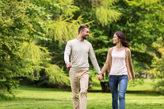 Concepto de amor, relación, familia y personas - pareja feliz caminando en el parque de verano