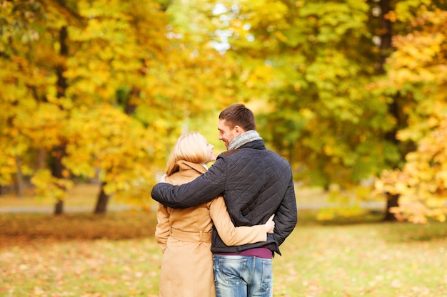 concepto de amor, relación, familia y personas - pareja sonriente abrazándose en el parque de otoño desde atrás