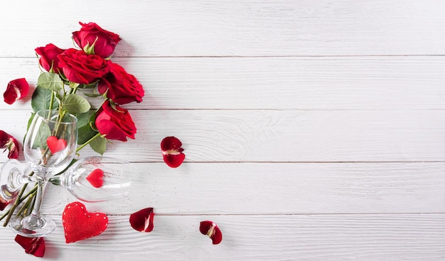 Concepto de amor y San Valentín hecho de copas de champán, vino, corazones rojos y rosa sobre fondo blanco de madera. Vista superior con espacio de copia, plano.