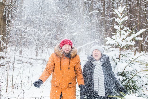 Concepto de amor, temporada, amistad y personas - feliz joven y mujer divirtiéndose y jugando con nieve en el bosque de invierno.