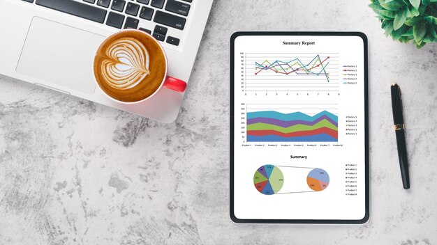 Concepto de análisis de negocios Un lugar de trabajo profesional con una tableta que muestra gráficos e informes acompañada de una computadora portátil una taza de café y un bolígrafo en una superficie de mármol