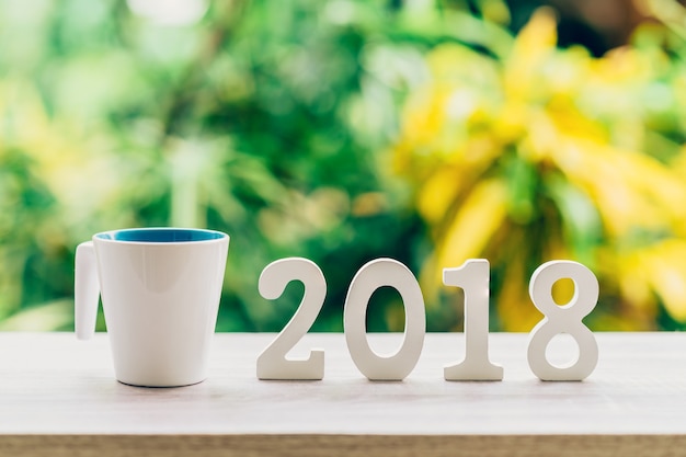 Concepto de Año Nuevo para 2018: Los números de madera 2018 en la mesa de madera y la taza de café con luz verde bokeh borroso de fondo.