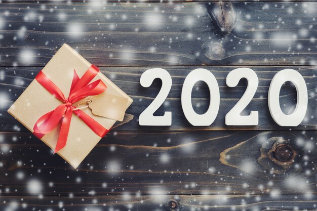 Concepto de año nuevo 2020: número de madera 2020 y caja de regalo marrón con nieve en el fondo de la tabla de madera.