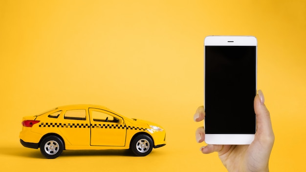 Foto concepto de aplicación móvil en línea de taxi urbano. juguete modelo taxi amarillo. mano que sostiene el teléfono inteligente con la aplicación de servicio de taxi en la pantalla.