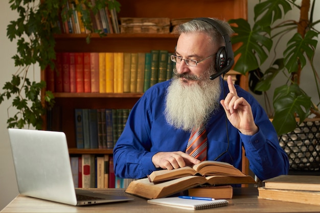 Concepto de aprendizaje a distancia. Profesor profesor tutor en auriculares enseña disciplina en línea. Hombre barbudo maduro responde a la pregunta del profesor a través de la computadora portátil.