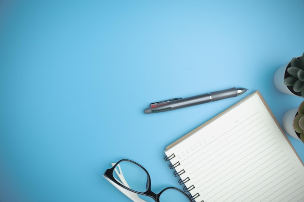 Concepto de aprendizaje de estudio de negocios El escritorio de oficina azul con un cuaderno, un bolígrafo y un mini árbol en el fondo plano del escritorio azul Vista superior del espacio de trabajo de la oficina de mesa con espacio de copia