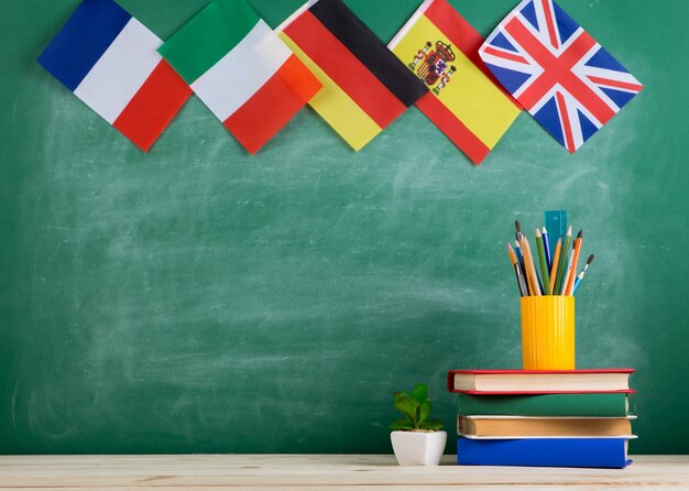 Concepto de aprendizaje de idiomas - banderas de España, Francia, Gran Bretaña y otros países, libros y cancillería en el fondo de la pizarra