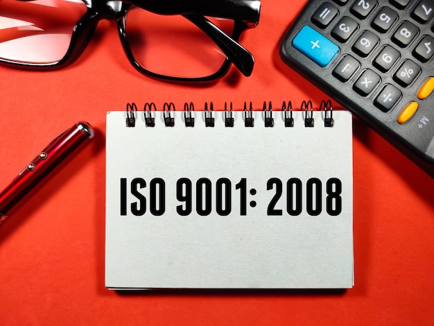 Concepto de aseguramiento de la calidad Texto ISO 90012008 escrito en un cuaderno con penglasses y calculadora