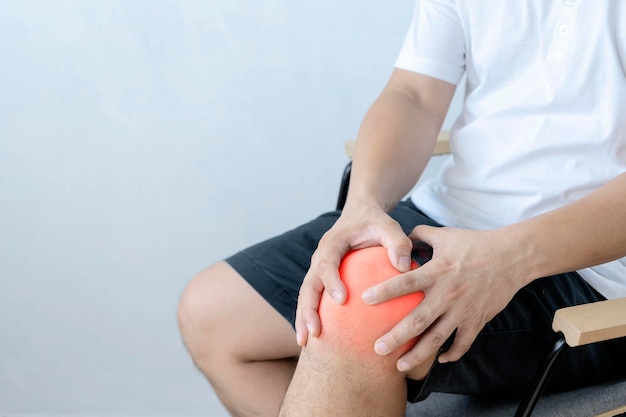 Concepto de atención médica Primer plano de un hombre sentado y sosteniendo su rodilla con dolor debido a una lesión en el fondo blanco