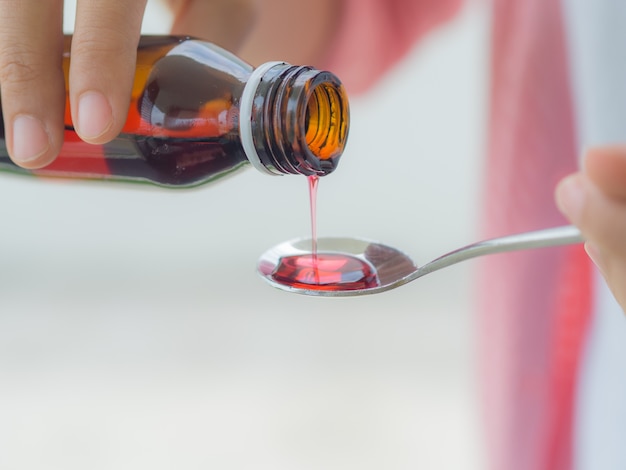 Foto concepto de la atención sanitaria - mujer que vierte el jarabe antipirético de la botella a la cuchara.