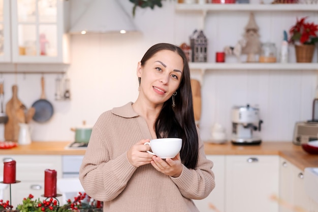 Concepto de atmósfera navideña festiva mujer linda bebiendo té o café en una cocina decorada