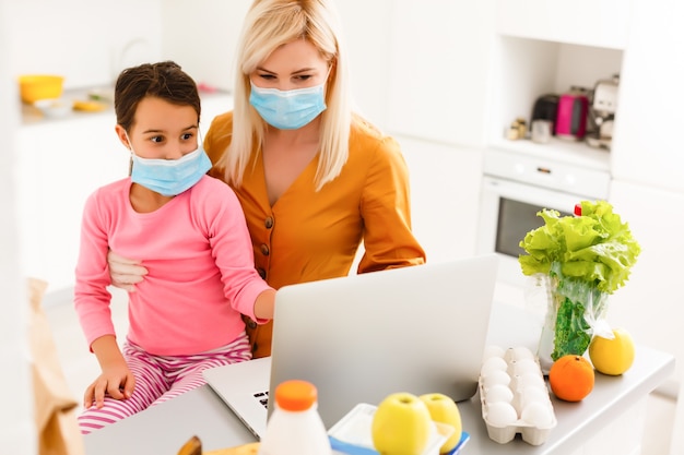 Concepto de autoaislamiento. Madre e hija desembalaje de la bolsa de papel con comida en la cocina, lista para la cuarentena durante el brote epidémico