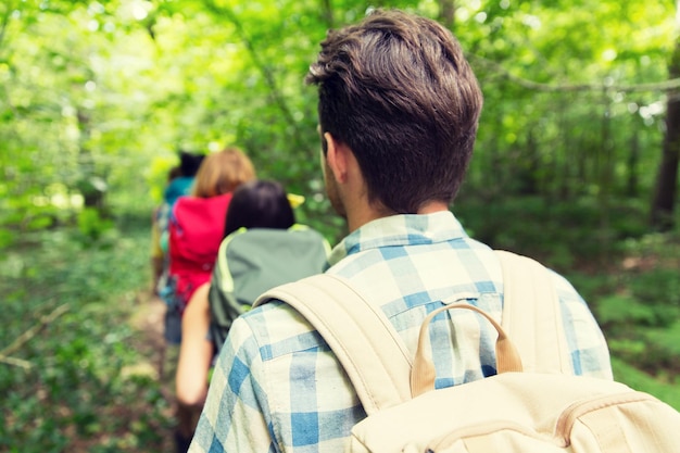 concepto de aventura, viajes, turismo, caminatas y personas: cerca de amigos caminando con mochilas en el bosque desde atrás