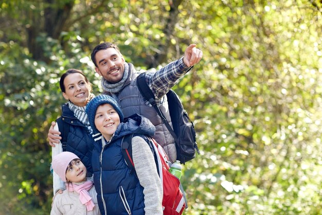 concepto de aventura, viajes, turismo, caminatas y personas - familia feliz caminando con mochilas en el bosque