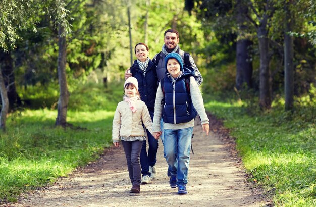 concepto de aventura, viajes, turismo, caminatas y personas - familia feliz caminando con mochilas en el bosque