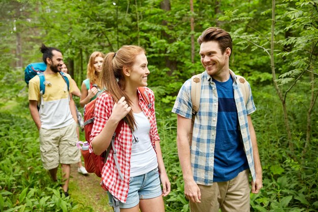 concepto de aventura, viajes, turismo, caminatas y personas - grupo de amigos sonrientes caminando con mochilas en el bosque