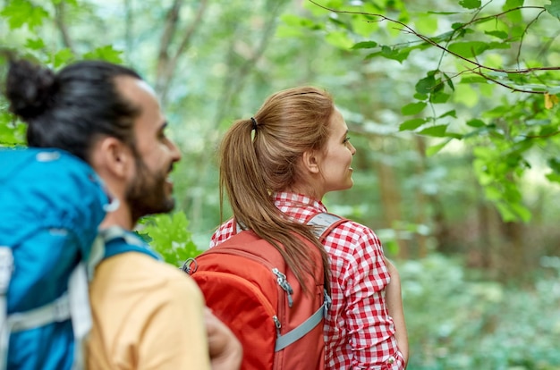 concepto de aventura, viajes, turismo, caminatas y personas - grupo de amigos sonrientes caminando con mochilas en el bosque