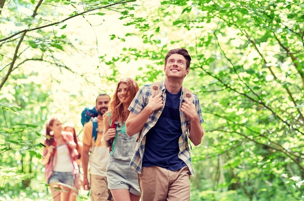 Foto concepto de aventura, viajes, turismo, caminatas y personas - grupo de amigos sonrientes caminando con mochilas en el bosque