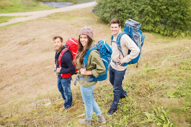 concepto de aventura, viajes, turismo, caminatas y personas - grupo de amigos sonrientes con mochilas al aire libre