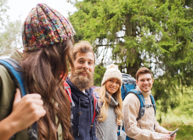 concepto de aventura, viajes, turismo, caminatas y personas - grupo de amigos sonrientes con mochilas y computadora de tablet pc caminando al aire libre