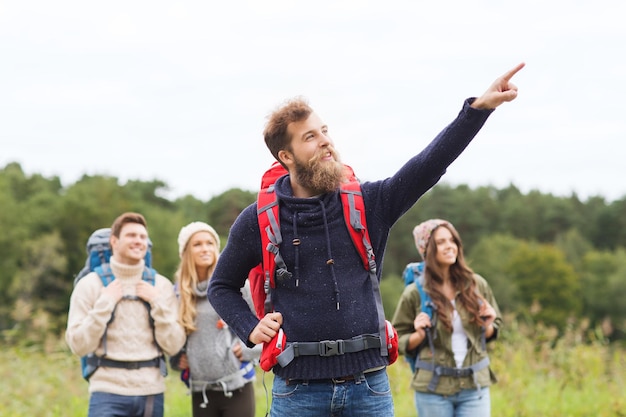 concepto de aventura, viajes, turismo, caminatas y personas - grupo de amigos sonrientes con mochilas señalando con el dedo al aire libre